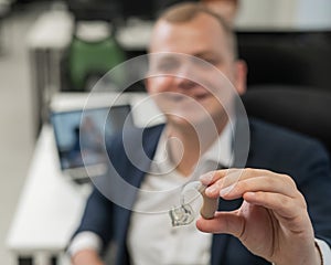 Deaf man working holds hearing aid while sitting in office.