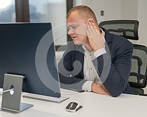 A deaf man works at a computer in the office. Broken hearing aid causing pain.