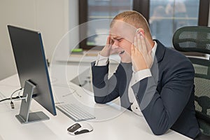 A deaf man works at a computer in the office. Broken hearing aid causing pain.