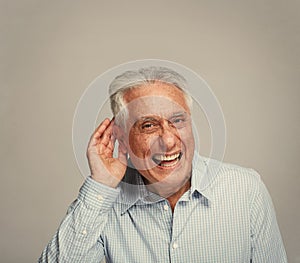 Deaf senior man holding hand near ear.