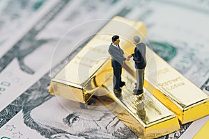 Deal or negotiation in investment, gold, wealth management concept, miniature people rich businessman shaking hand on gold bar, b