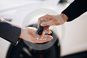 Dealer giving key to new owner in auto show or salon. Male hand gives a car keys to male hand in the car dealership