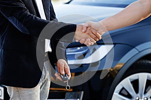 Dealer giving key to new owner in auto show or salon. Male hand gives a car keys to male hand in the car dealership