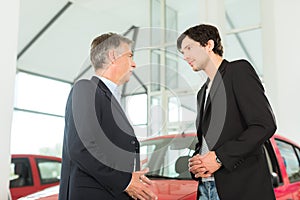 Dealer and young man with auto in car dealership