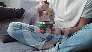 Dealing with depression and stress. Young man using tibetan singing bell bowl at living room. Carrying about mental