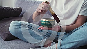 Dealing with depression and stress. Young man using tibetan singing bell bowl at living room. Letters mean tibetan