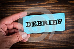 DEBRIEF concept. Blue paper sheet with text in man& x27;s hands, wooden texture background