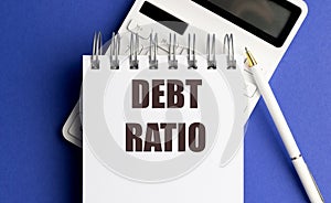 Debt ratio written on spiral notebook with calculator and pen on blue background
