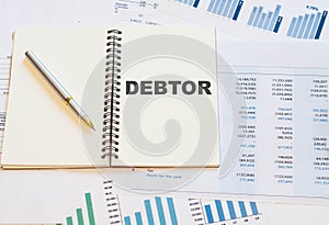 DEBTOR on an open notebook with a pen and financial papers