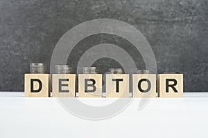 debtor word, text written on wooden cubes on a black background with coins on cubes