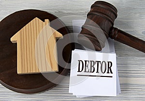 DEBTOR - word on a white sheet against the background of a judge`s hammer and a wooden house