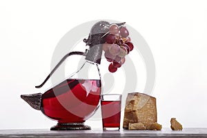 A decanter of red wine, a glass of wine, expensive cheeses, cheese with mold, black cheese and grapes.