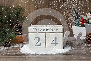 December 24 - Christmas Eve. Snow falling onto wooden block calendar and festive decor on table