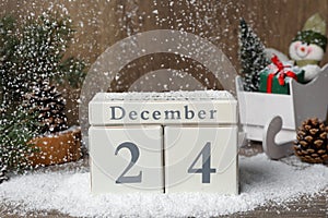 December 24 - Christmas Eve. Snow falling onto wooden block calendar and festive decor on table