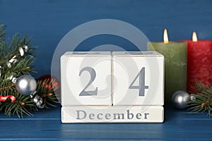 December 24 - Christmas Eve. Wooden block calendar and festive decor on blue table