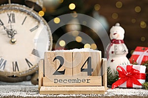 December 24 - Christmas Eve. Wooden block calendar, watch and festive decor on table against blurred lights