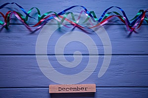 December message on wooden plank with multicolored streamer on blue wooden background