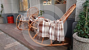 Wicker cozy armchair with blanket and small glass table outdoors. Plaid lies on the wicker furniture from rattan.