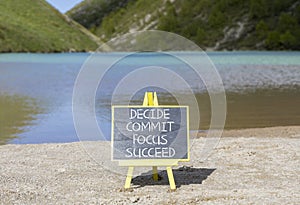 Decide commit focus succeed symbol. Concept word Decide Commit Focus Succeed on beautiful blackboard. Beautiful mountain lake