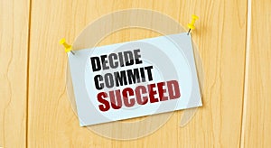 DECIDE COMMIT SUCCEED sign written on sticky note pinned on wooden wall