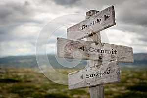 Decide commit and succeed text on wooden rustic signpost outdoors in nature/mountain scenery.