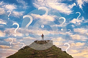 A decision concept. Of a man standing o n top of a hill. With question marks floating in the sky. With an artistic edit