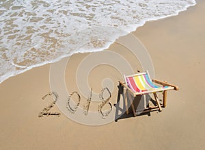 Deck chair with 2018 written in sand write on beach.