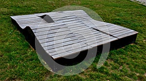 Deck chair composed of three waves which are made of wood and board. large seating elements in a landscape park. furniture for ten