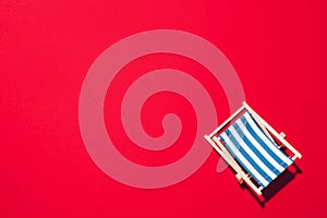 Deck chair with hard shadow on red paper background. Flat lay and copy space. Summer travel vacation concept. Minimal composition