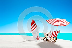 Deck chair under an umbrella with a surfboard on sandy beach by the sea and sky with copy space