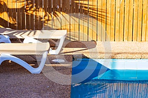 Deck chairs near swimming pool site rustic relaxation space on villa back yard sunny lighting shadow from palm on background