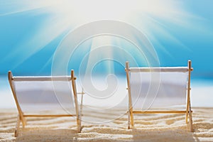 Deck chairs on sandy beach with blurry blue ocean and sun beams on sky. Social distancing or COVID-19 protection at summer