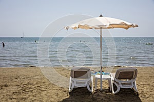 Deck chairs and umbrella on a sandy beach, sea water background