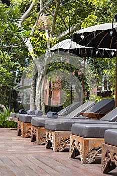 Deck chairs and umbrellas in tropical garden near swimming pool on the beach in Bali, Indonesia