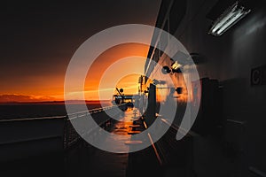 Deck of ferry sailing across the sea during last moments of a beautiful sunset with arriving land in the background. Concept of