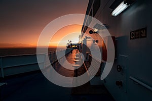 Deck of ferry sailing across the sea during last moments of a beautiful sunset with arriving land in the background. Concept of