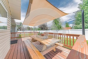 Deck of a house with wooden chairs and table under a shade sail