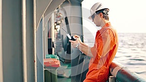 Deck Officer on deck of offshore vessel holds VHF walkie-talkie radio