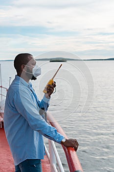 Deck officer with protective mask on the deck of a ship or offshore vessel. You have in your hands a VHF walkie-talkie radio