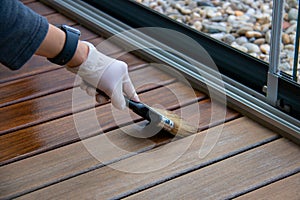 Deck staining, worker applying deck oil on decking boards with paint brush