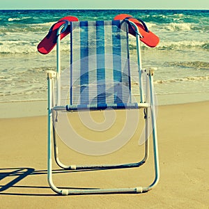 deckchair and orange flip-flops on the beach, with a retro effect