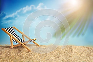 Deckchair and palm on the sandy beach. Summer time.