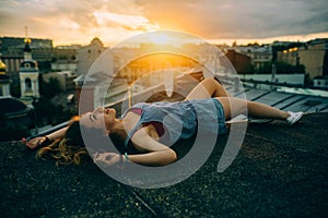 Beautiful woman rests on the roof view from the back, sunset time, city, rest time, light, hipster photo, brunette hair