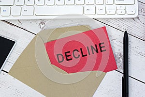 Decline text on red card with envelope, white keyboard and pen on wooden table.