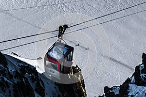Decommisioned cable car hanging from cables over skiers traversing glacier below on trodden path.