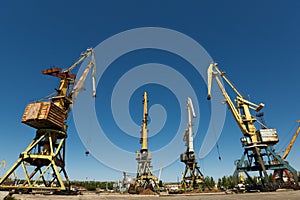 Decommissioned harbor cranes stand idle in disrepair at derelict seaport. Rusting machinery industry decline. Potential