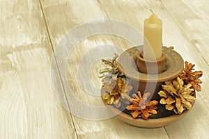 Decor elements for Christmas. Handmade clay candlestick, wax candle and fir cones on light wooden background.