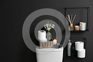 Decor elements, necessities and toilet bowl near black wall, space for text. Bathroom photo