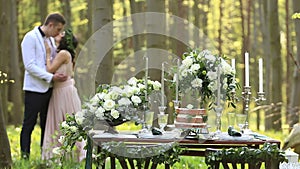 Decor romantic dinner for lovely couple in love in the green spring forest. Beautiful bride and groom kiss and feel
