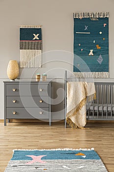 Decor on the wall above grey cabinet and child`s bed with blanke